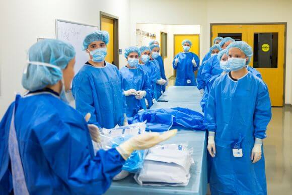 Healthcare workers in full surgical attire listen to an instructor