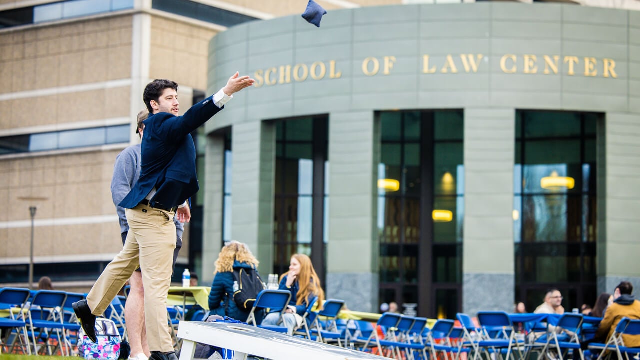 A person plays a lawn game on a grassy area in front of the Law Center set up with tables and chairs