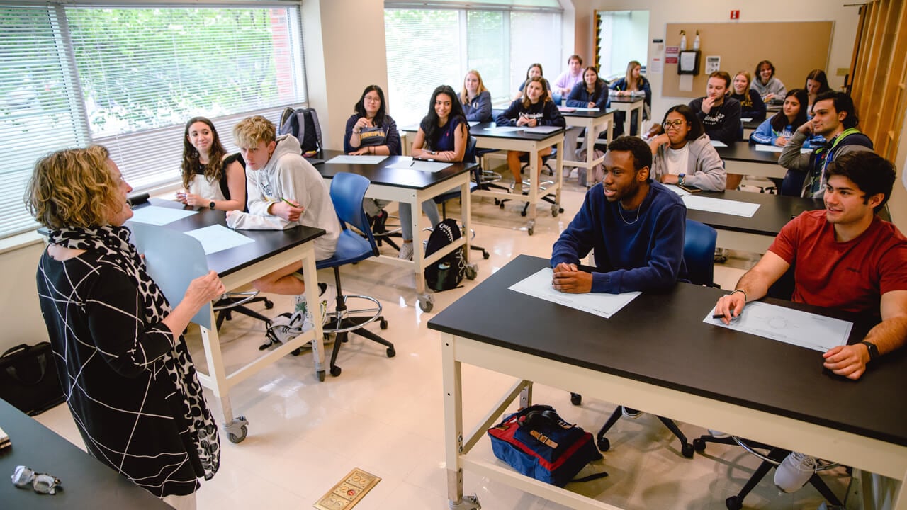 Two rows of tables with people seated listening to a presenter