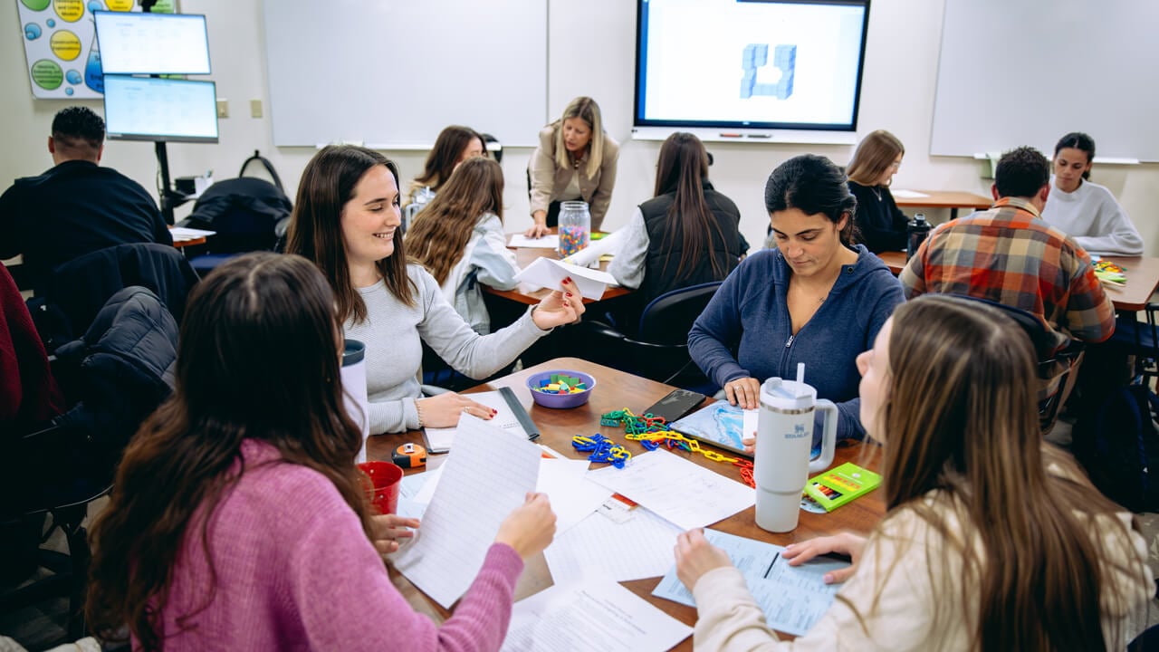 Groups of people collaborate at tables with projector screens behind them