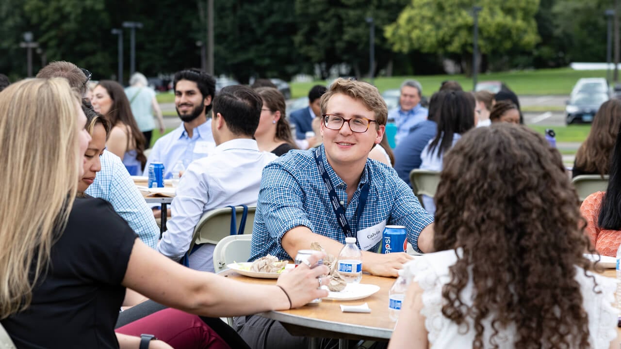 A group of people network seated at tables on a lawn