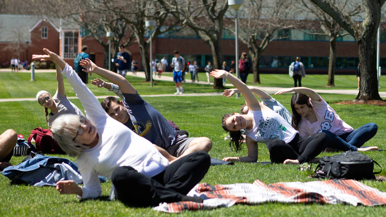 A small group of people do yoga on the Quinnipiac quad on a sunny day