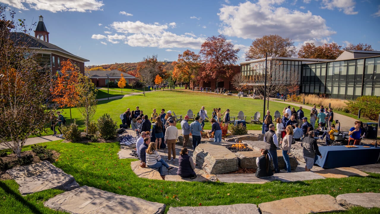 Dozens of people interact in the outdoor amphitheater in front of the recreation center with the clocktower behind them